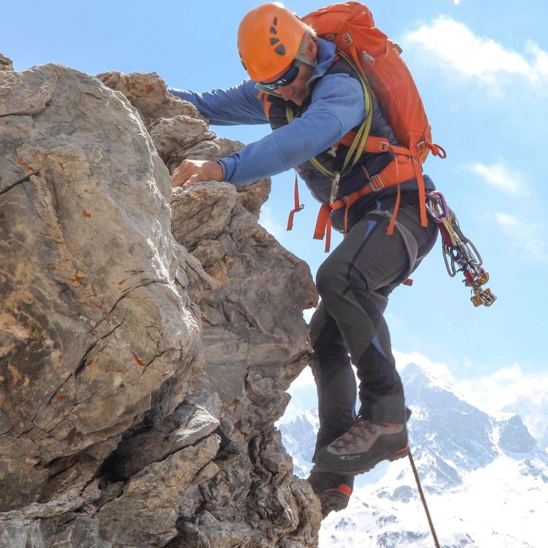 Person climbing a rocky mountain peak with safety gear